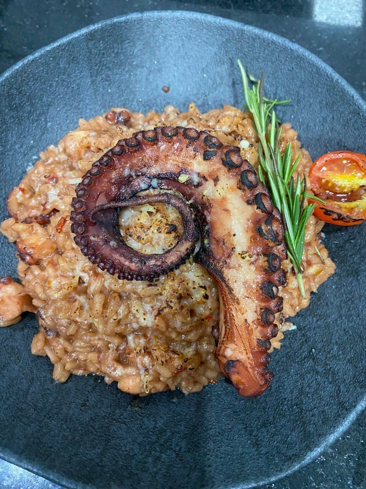 Un plato de comida con tentáculos de pulpo y una rodaja de tomate, adornado con romero.