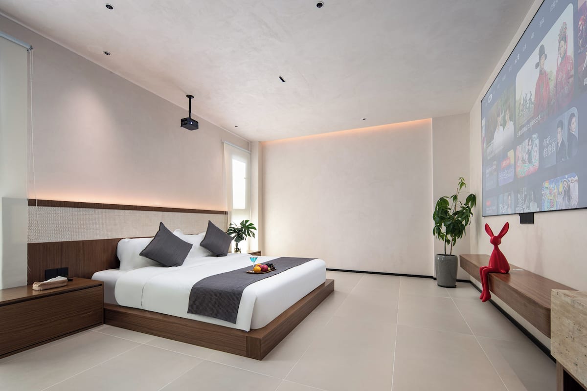 Un dormitorio moderno con una cama grande, mesitas de noche, una planta en maceta y un televisor montado en la pared.