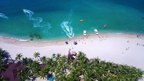 A beach with clear turquoise water, boats, and palm trees. - Sanya Qixili Hotel - Free two wheeled electric bike ride around the island (Sanya)