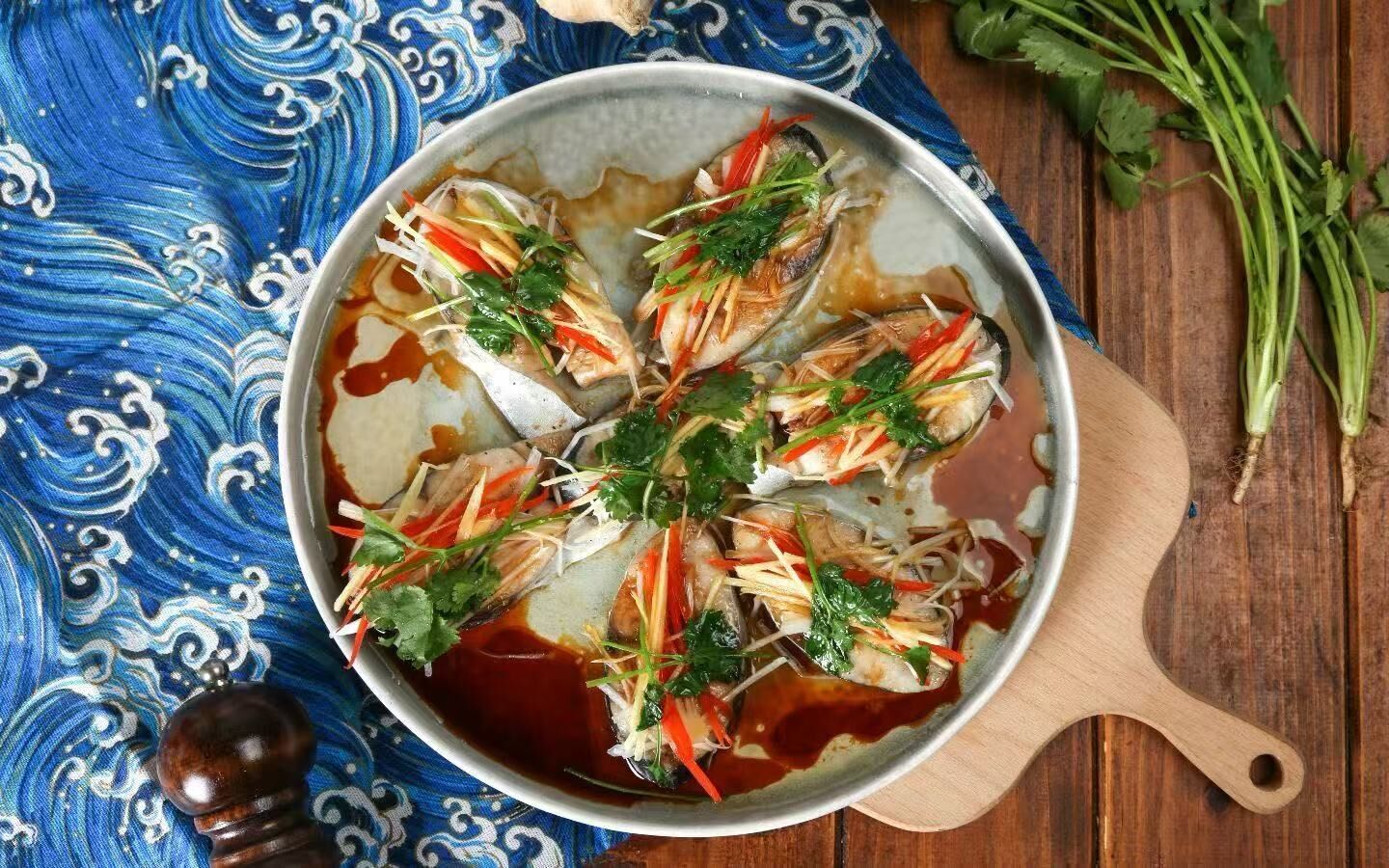 A pan with fish and vegetables on a wooden board.