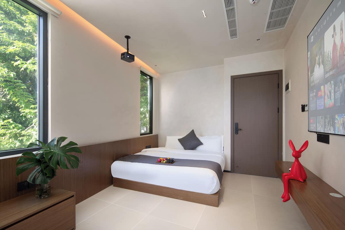 Un dormitorio moderno con una cama grande, una mesita de noche, una planta en maceta y una escultura roja.