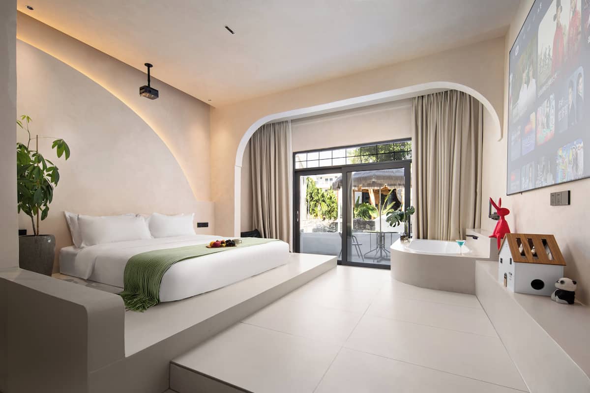 Una habitación de hotel moderna con una cama grande, una bañera y un balcón con cortinas.