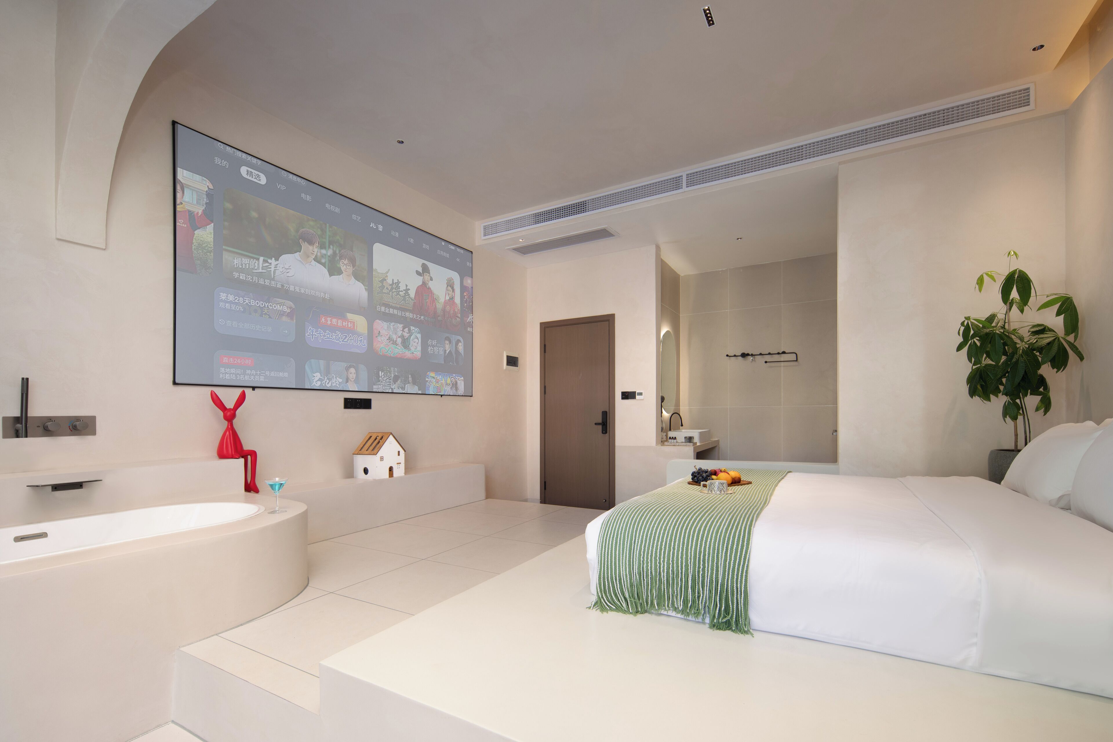 A modern hotel room with a large bed, a bathtub, and a flat-screen TV mounted on the wall.