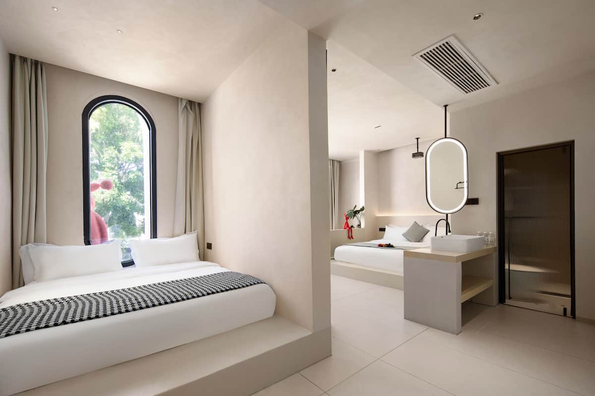 Una habitación de hotel moderna con una cama grande, un baño con tocador y un ventanal amplio.