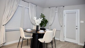 Et spiseområde med et rundt bord, fire stole, en vase med hvide blomster og en potteplante.