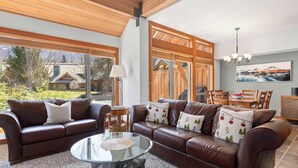A spacious living area with a brown leather sofa, a glass coffee table, and a dining area with wooden furniture.
