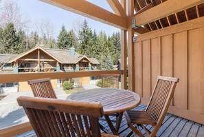 A wooden deck with a round table and chairs, overlooking a building with a sloped roof. - Village North townhouse w/ hot tub (Whistler)
