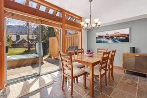 Un coin repas avec une table et des chaises en bois, un lustre, un tableau au mur et une vue sur un jardin avec un jacuzzi.