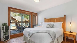 A bedroom with a large bed, a nightstand, a lamp, a sliding glass door leading to an outdoor area with a chair and table.