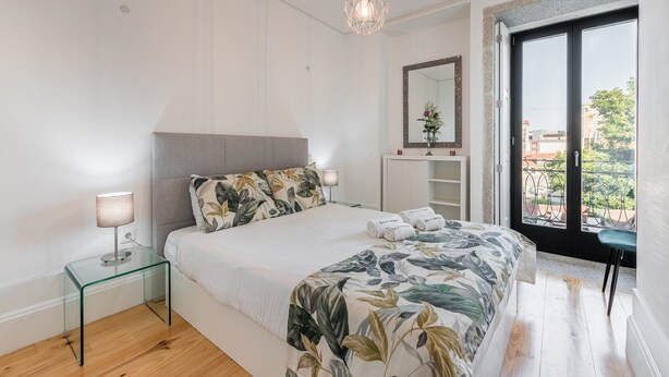 A modern bedroom with a bed, bedside table, and a view of the outside. - GuestReady - Rose Apartment (Porto)