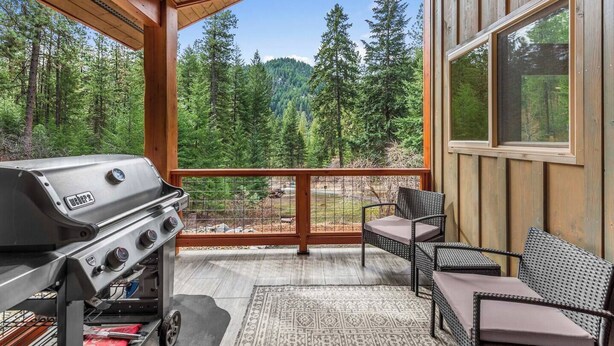 A balcony with a grill, wicker furniture, and a view of a forested area. - Eagle Creek Hideaway (Leavenworth)
