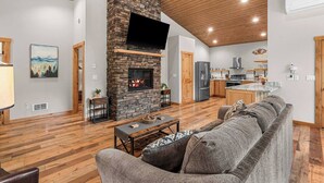 A spacious living area with a stone fireplace, wooden flooring, and a kitchen in the background. - Eagle Creek Hideaway (Leavenworth)