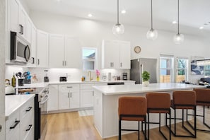 A modern kitchen with white cabinetry, a large island with bar stools, and pendant lighting. - Sleek 4br/3ba Urban Living w/ Downtown Views! (San Antonio)