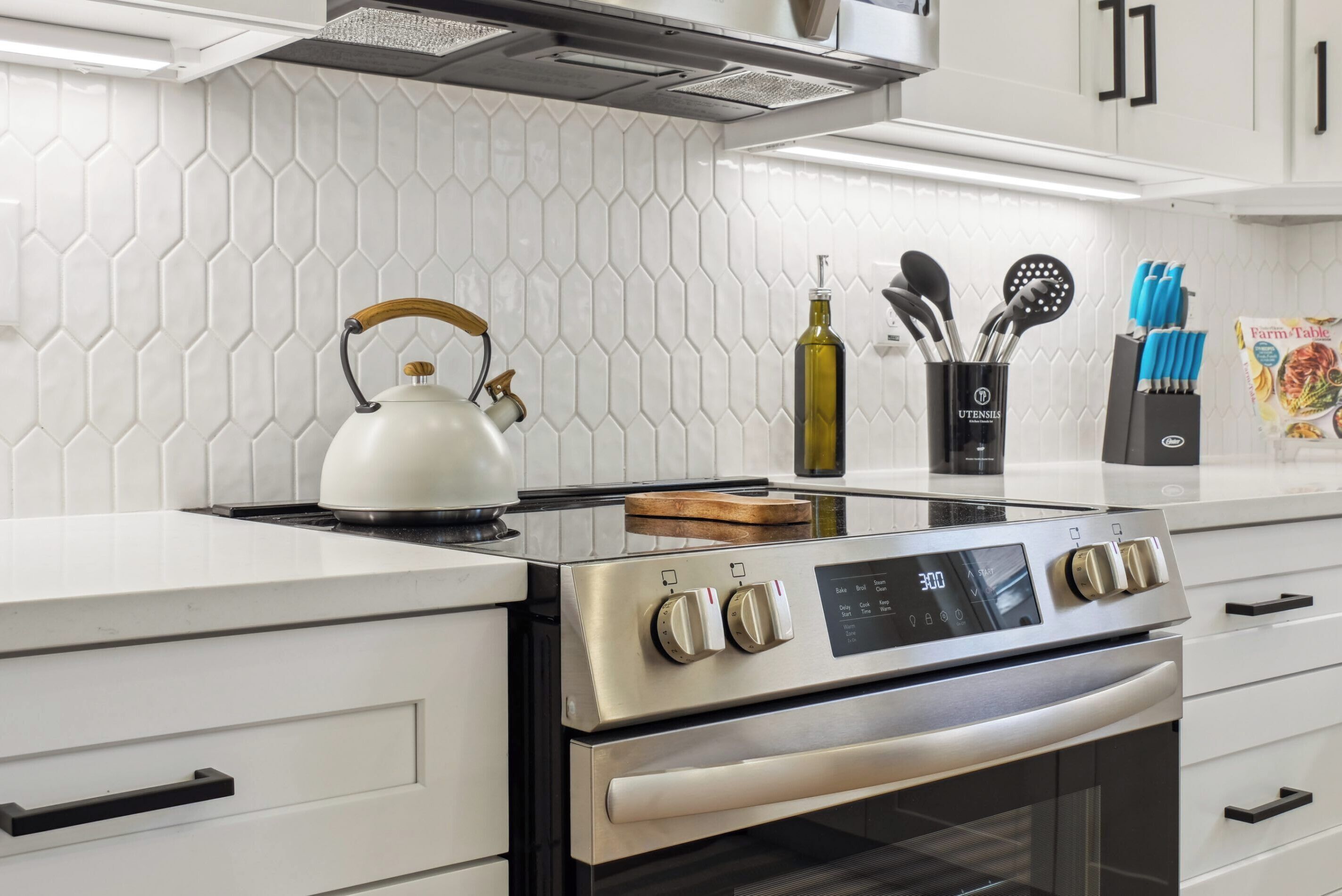 Una cocina moderna con estufa de acero inoxidable, muebles blancos y un salpicadero de azulejos hexagonales.