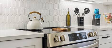 Una cocina moderna con estufa de acero inoxidable, muebles blancos y un salpicadero de azulejos hexagonales.