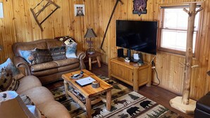 A cozy living room with a brown leather couch, a wooden coffee table, a TV on a stand, and a bear-themed rug.