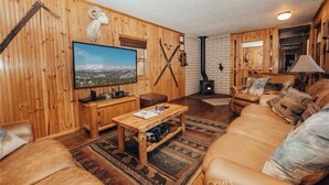 A cozy cabin interior with wooden walls, a fireplace, a television, and leather furniture.