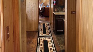 A wooden hallway with a patterned rug, a fire extinguisher, and a kitchen area with wooden cabinets.