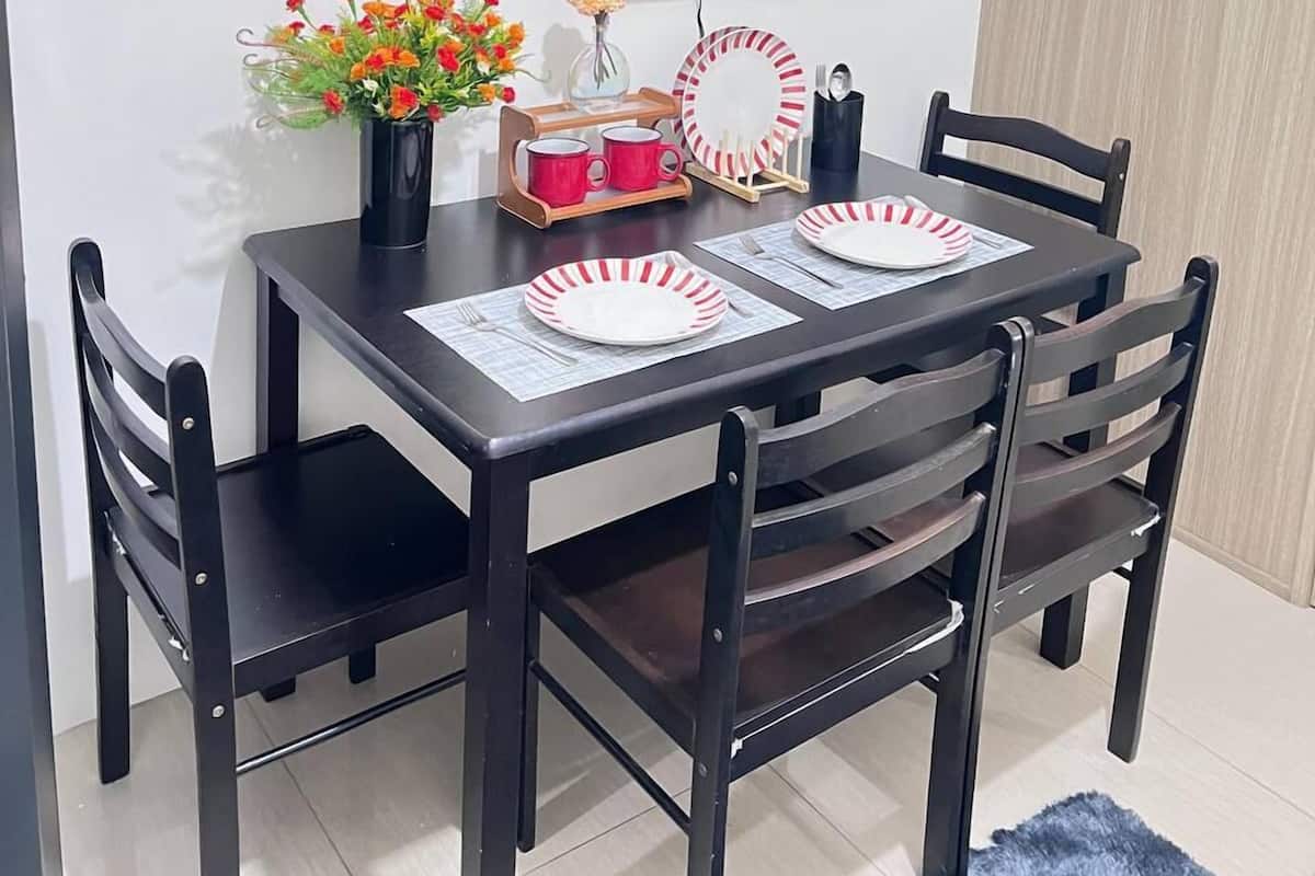 Un coin repas avec une table noire dressée pour quatre personnes, entourée de chaises en bois foncé. Un téléviseur à écran plat est fixé au mur, au-dessus de la table.