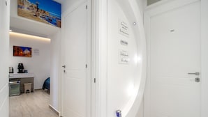 Un couloir d’hôtel avec des portes blanches, un distributeur de café, une poubelle et un tableau accroché au mur.