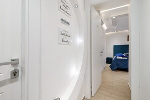 Un pasillo con una puerta, una cama con cabecera azul y una pared con letreros.