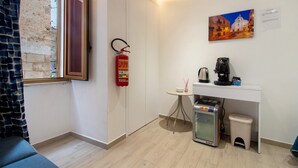 A compact room with a kitchenette, a fire extinguisher, a small table, a radiator, and a window with a view of a building. - Room 'Il Filo Di Arianna - Camera 2' with Wi-Fi and Air Conditioning (Bari)