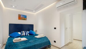 A bedroom with a bed, pillows, a painting, an air conditioner, and a door. - Room 'Il Filo Di Arianna - Camera 2' with Wi-Fi and Air Conditioning (Bari)
