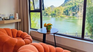 A modern room with large windows overlooking a river and mountains, featuring orange furniture and a small table with flowers. - Xiang Zhu Zi Yuan (Guilin)