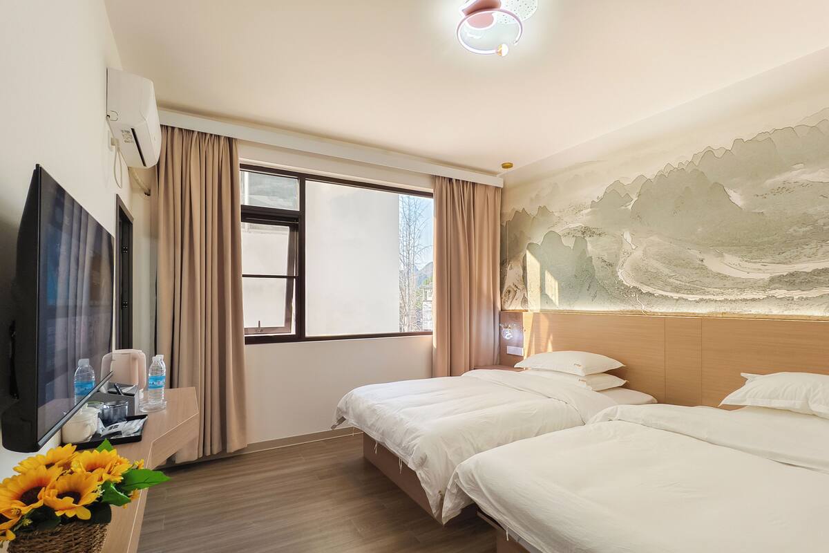 A hotel room with two beds, a TV, a desk with a lamp, and a window with curtains.