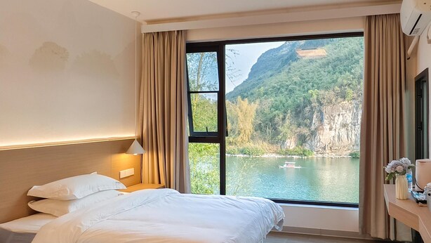A hotel room with two beds, a large window with a view of a lake and mountains, and a wooden floor. - Xiang Zhu Zi Yuan (Guilin)
