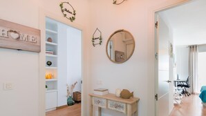 A hallway with a wooden floor, a white wall with a 'HOME' sign, a mirror, and a console table with decorative items.