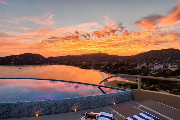 Una piscina infinita en la azotea con vista a la ciudad al atardecer.