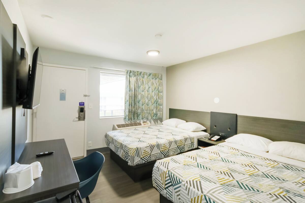A hotel room with two beds, a desk, a chair, a TV, and a window with curtains.