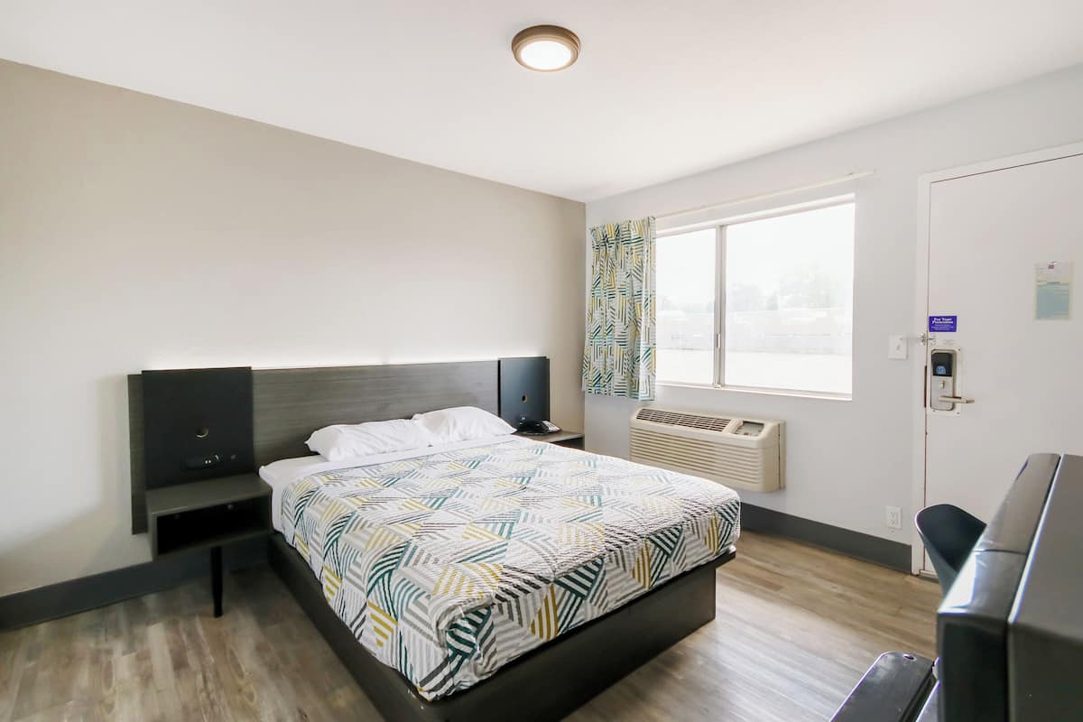 A modern hotel room with a large bed, a bedside table, a desk, and a window with curtains.