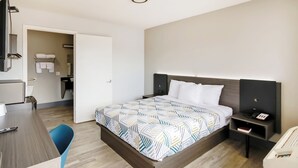 Une chambre d’hôtel comprenant un lit, une table de chevet et un bureau avec une chaise.