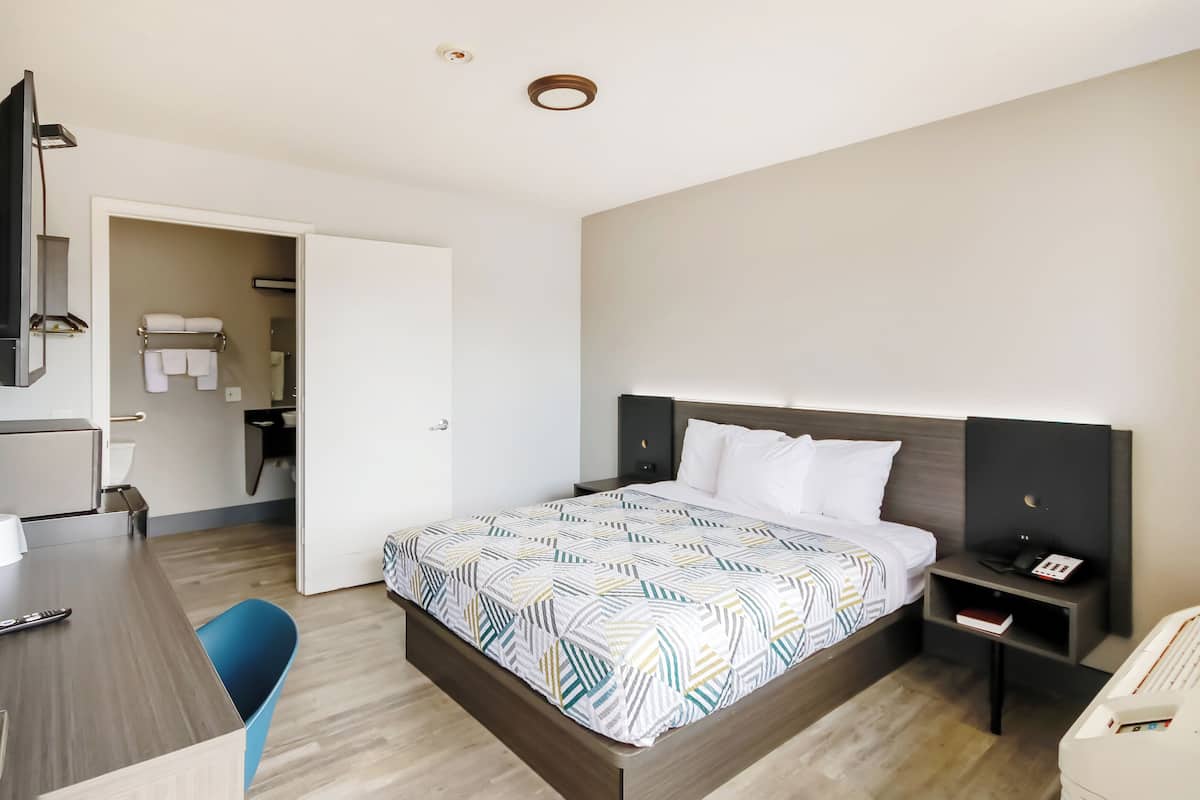 A hotel room with a bed, bedside table, and a desk with a chair.