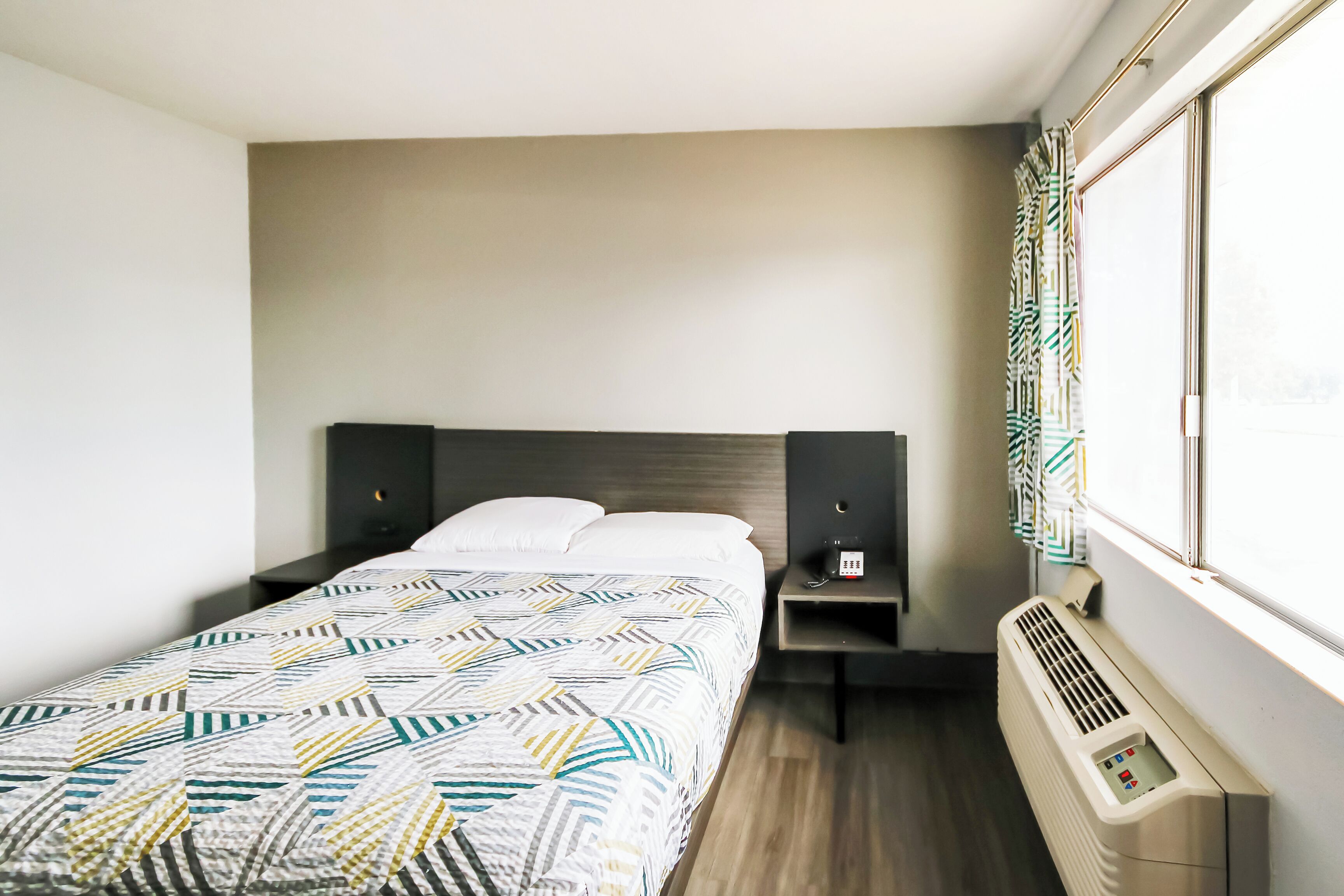 A hotel room with a bed, bedside tables, a heater, and a window with curtains.