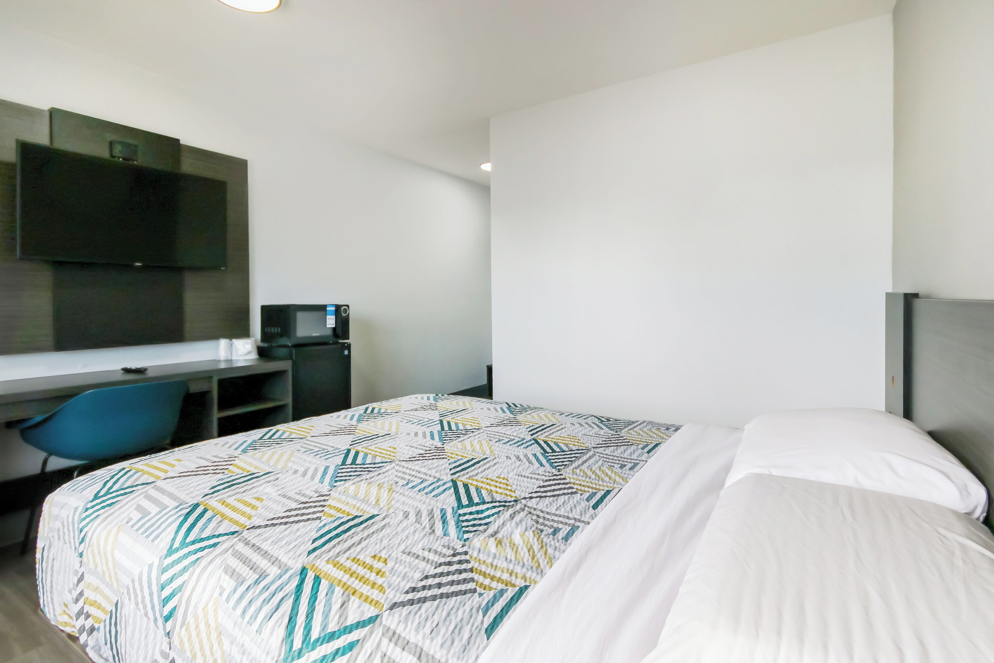 A hotel room with a bed, a desk with a chair, a television, and a flat-screen TV mounted on the wall.