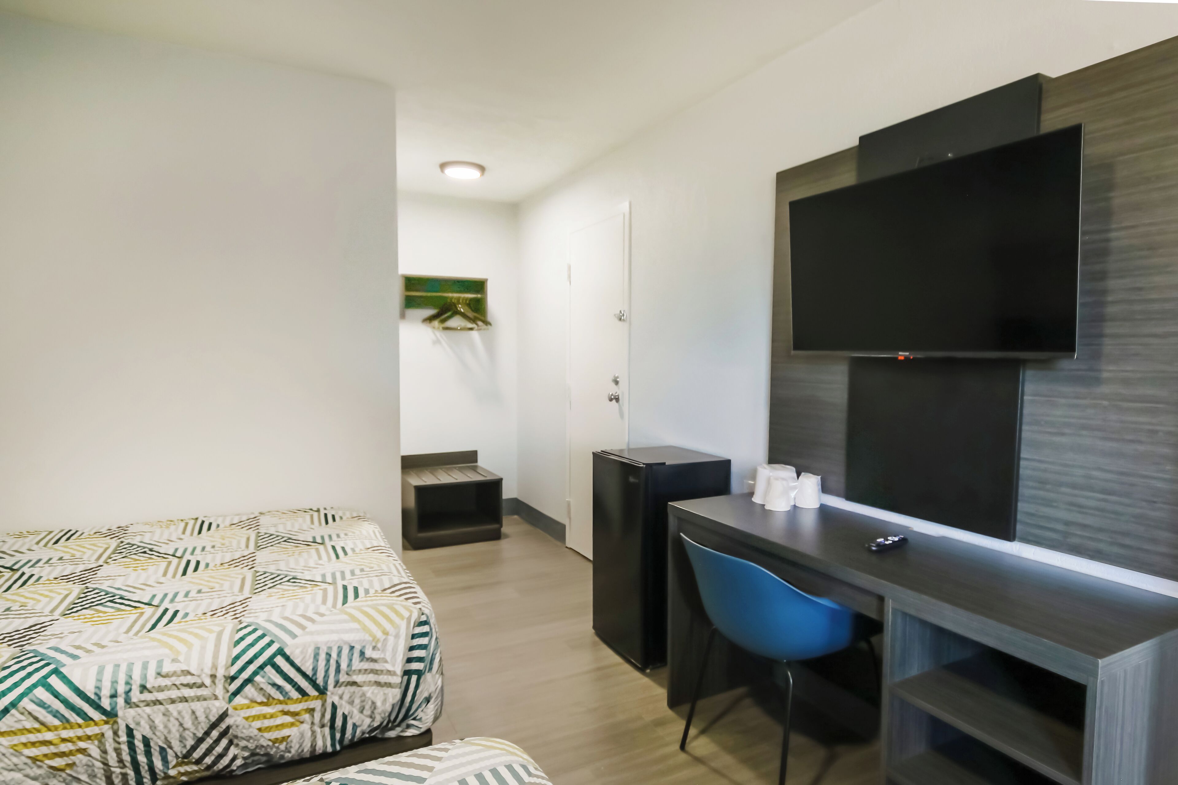 Een kleine hotelkamer met een bed, een bureau met stoel, een televisie en een kleine koelkast.