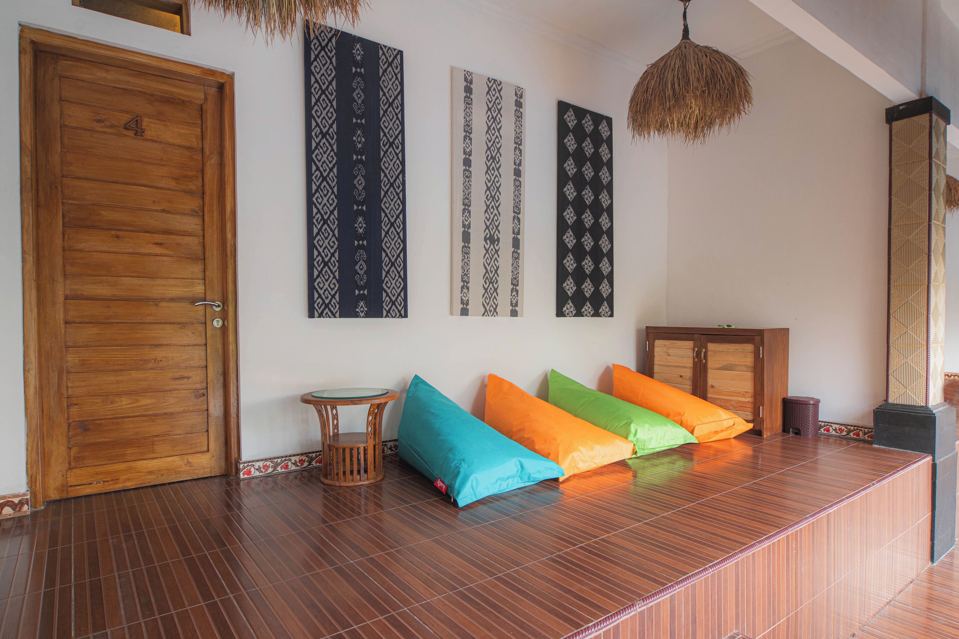 A room with a wooden door, a small round table, colorful cushions, and patterned wall hangings.