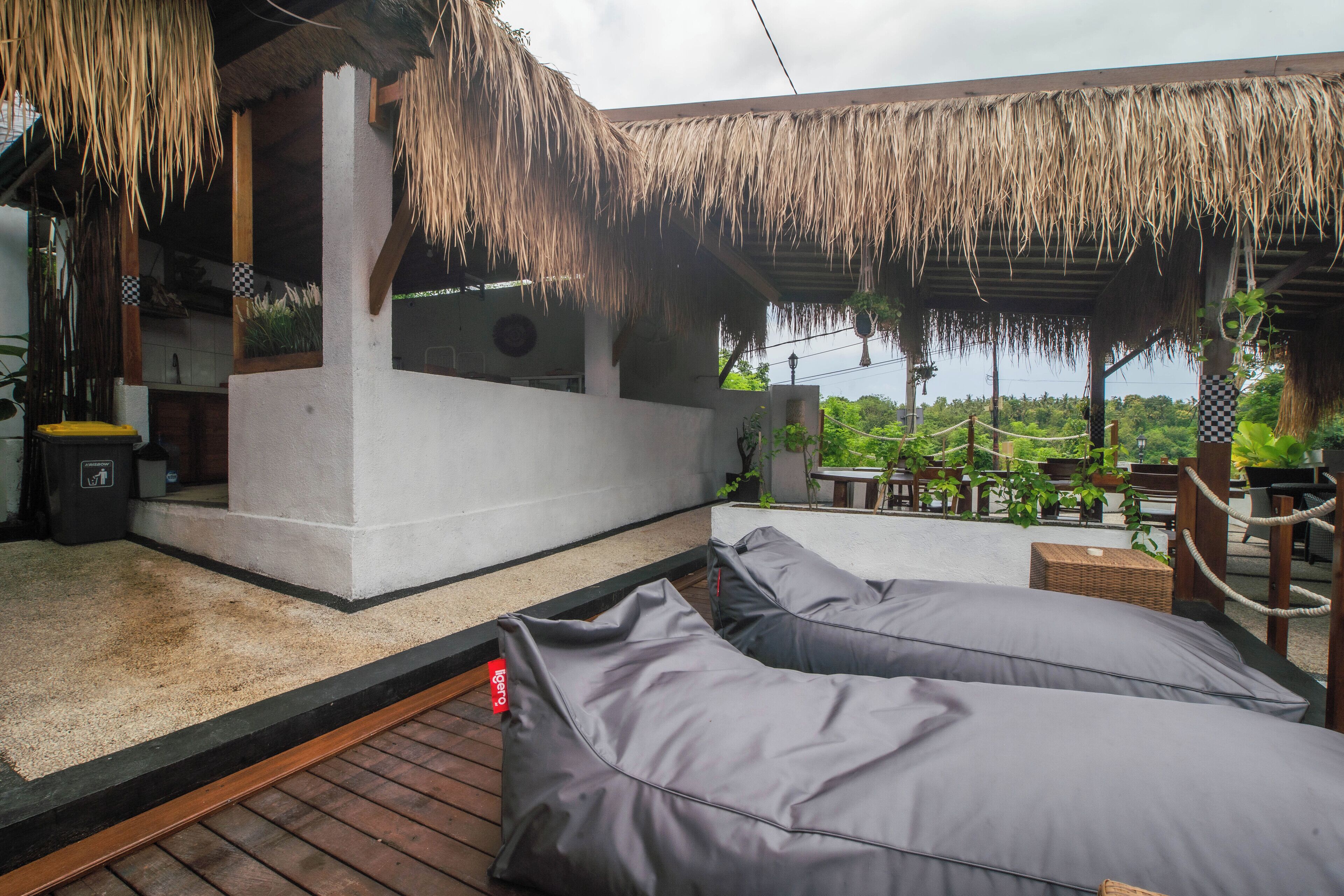 A covered outdoor seating area with thatched roof, a concrete bench, and a trash bin.