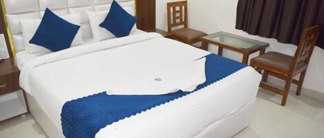 A neatly made bed with white and blue bedding, a wooden chair, a small glass table, and a brown rug.