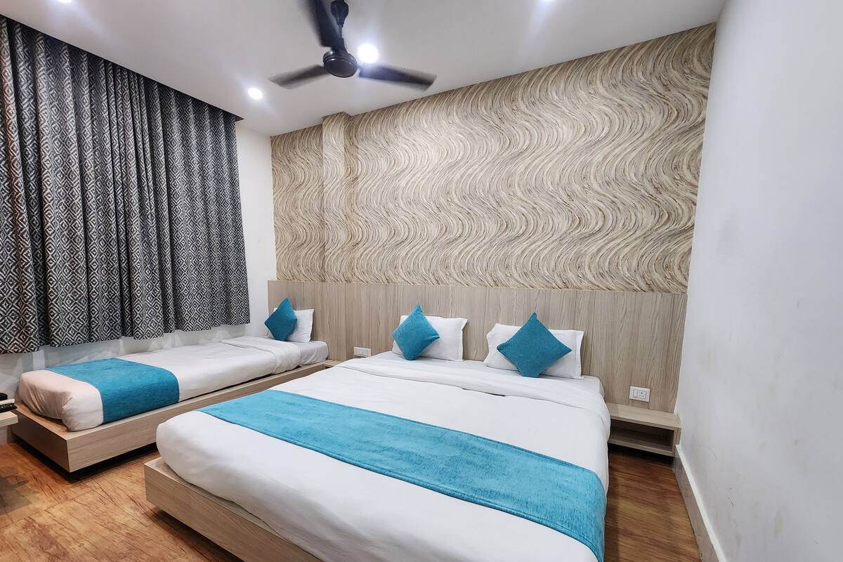 A hotel room with two beds, a ceiling fan, patterned curtains, and a textured wall.