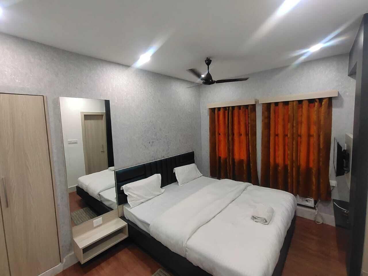 A bedroom with a bed, a wardrobe, a mirror, a ceiling fan, and curtains.