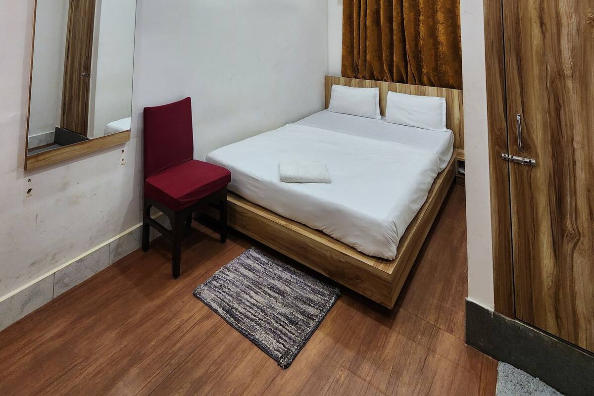 A modern bedroom with a wooden bed frame, a red chair, a large mirror, and a wardrobe.