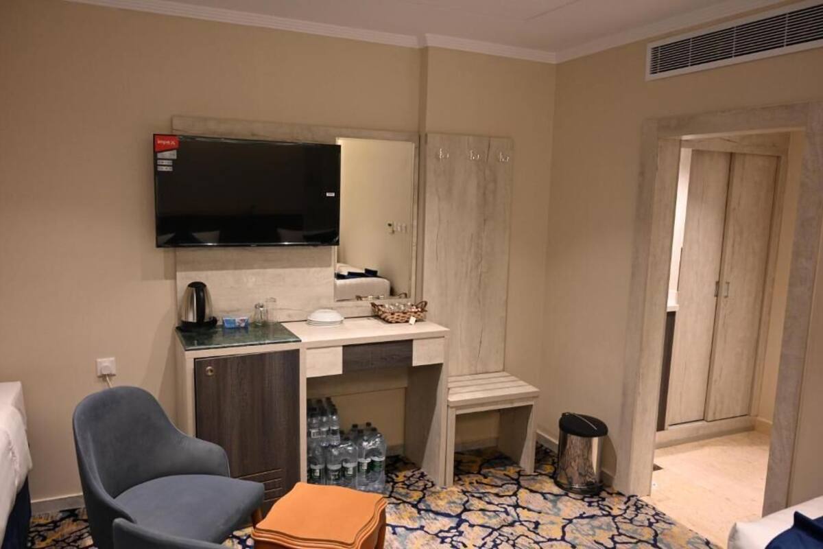 Hotellihuone, jossa on seinälle asennettu taulutelevisio pesualtaan yläpuolella, minibaari, tuoli, pieni pöytä ja roskakori.