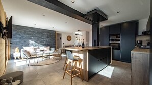 A modern kitchen with a central island, dark cabinetry, and a dining area with a round table and chairs. - Sylodges 202 - Spacious apartment for 10/12 people (LA TOUSSUIRE)