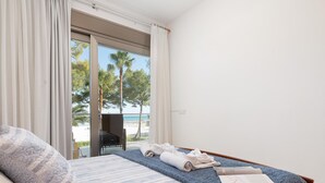 Una habitación de hotel con una cama, vistas a la playa y una silla junto a la ventana.
