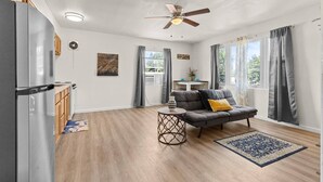 A compact living space with a kitchenette, a ceiling fan, a sofa with cushions, a small table, and a rug.