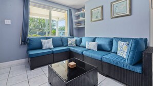 A room with a blue sectional sofa, a glass coffee table, and a window with curtains. - Waterfront Angler’s Paradise, 3BR/2.5BA w/ Dock, Boat Ramp, Kayaks, HorseShoes, CornHole, Ping Pong (New Port Richey)